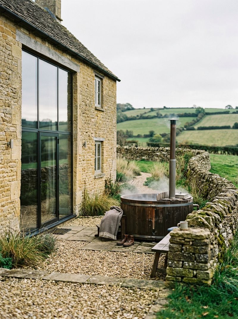A Cotswold stone cottage with a wood-fired hot tub on a gravel terrace